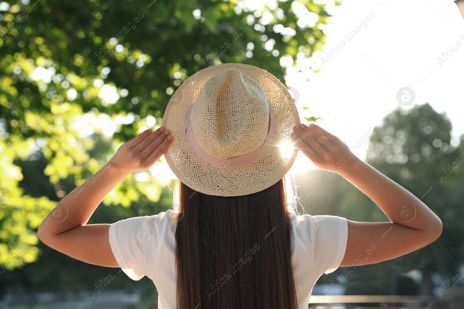 Photo of Young woman in hat outdoors on sunny day, back view