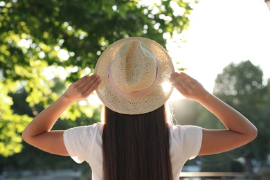 Photo of Young woman in hat outdoors on sunny day, back view