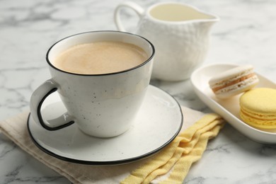 Photo of Tasty cappuccino in cup, macarons and saucer on white marble table, closeup