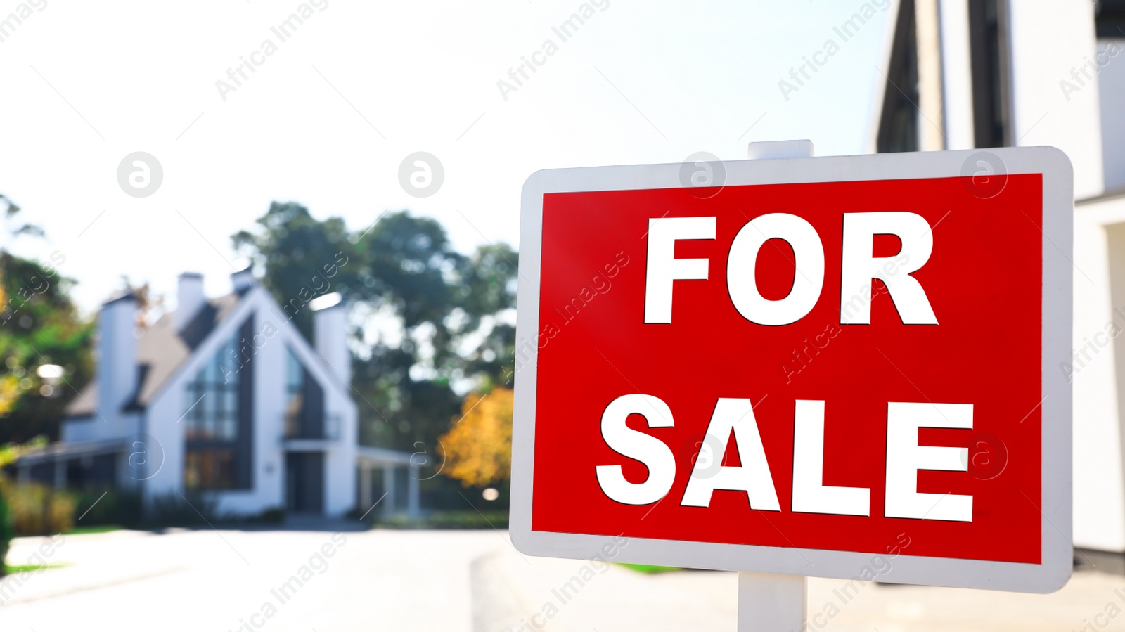 Photo of Red real estate sign near house outdoors on sunny day