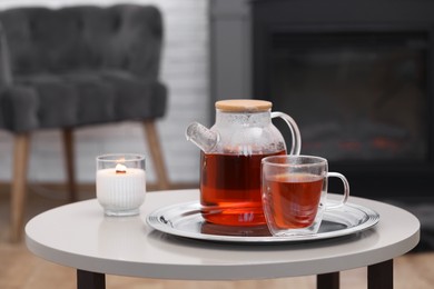 Teapot, cup of aromatic tea and burning candle on white table in room