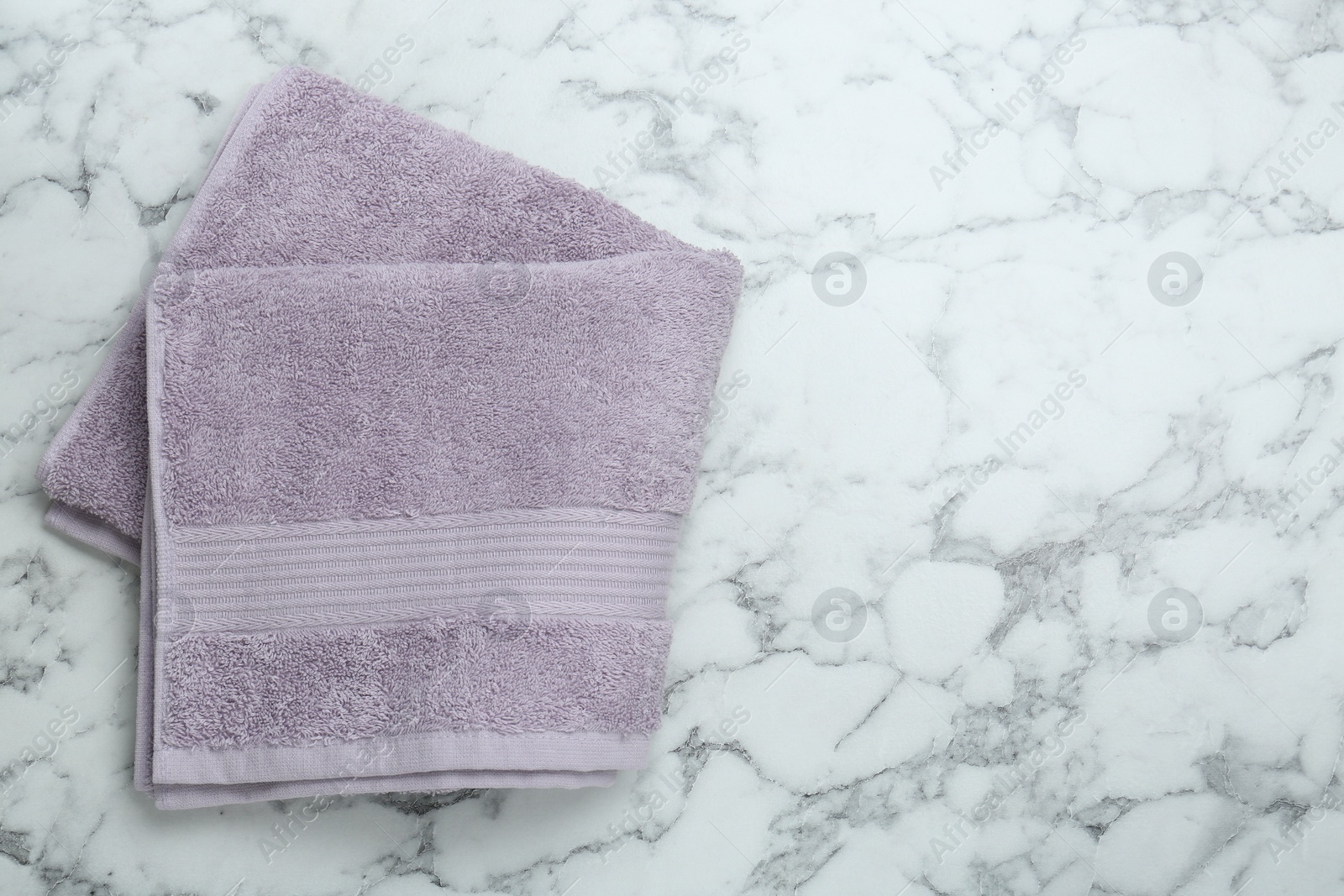 Photo of Violet terry towel on white marble table, top view. Space for text