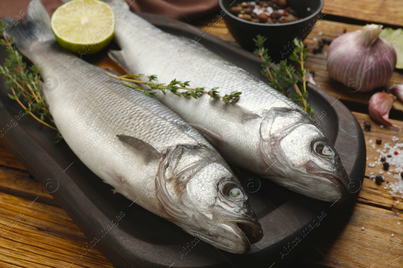 Photo of Sea bass fish and ingredients on wooden table, closeup