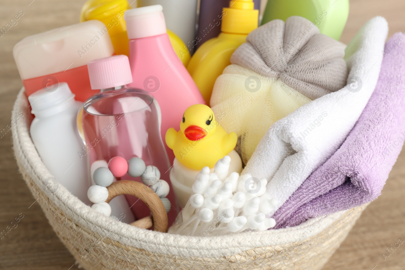 Photo of Wicker basket full of different baby cosmetic products, bathing accessories and toys on wooden table, closeup