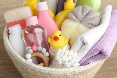 Photo of Wicker basket full of different baby cosmetic products, bathing accessories and toys on wooden table, closeup