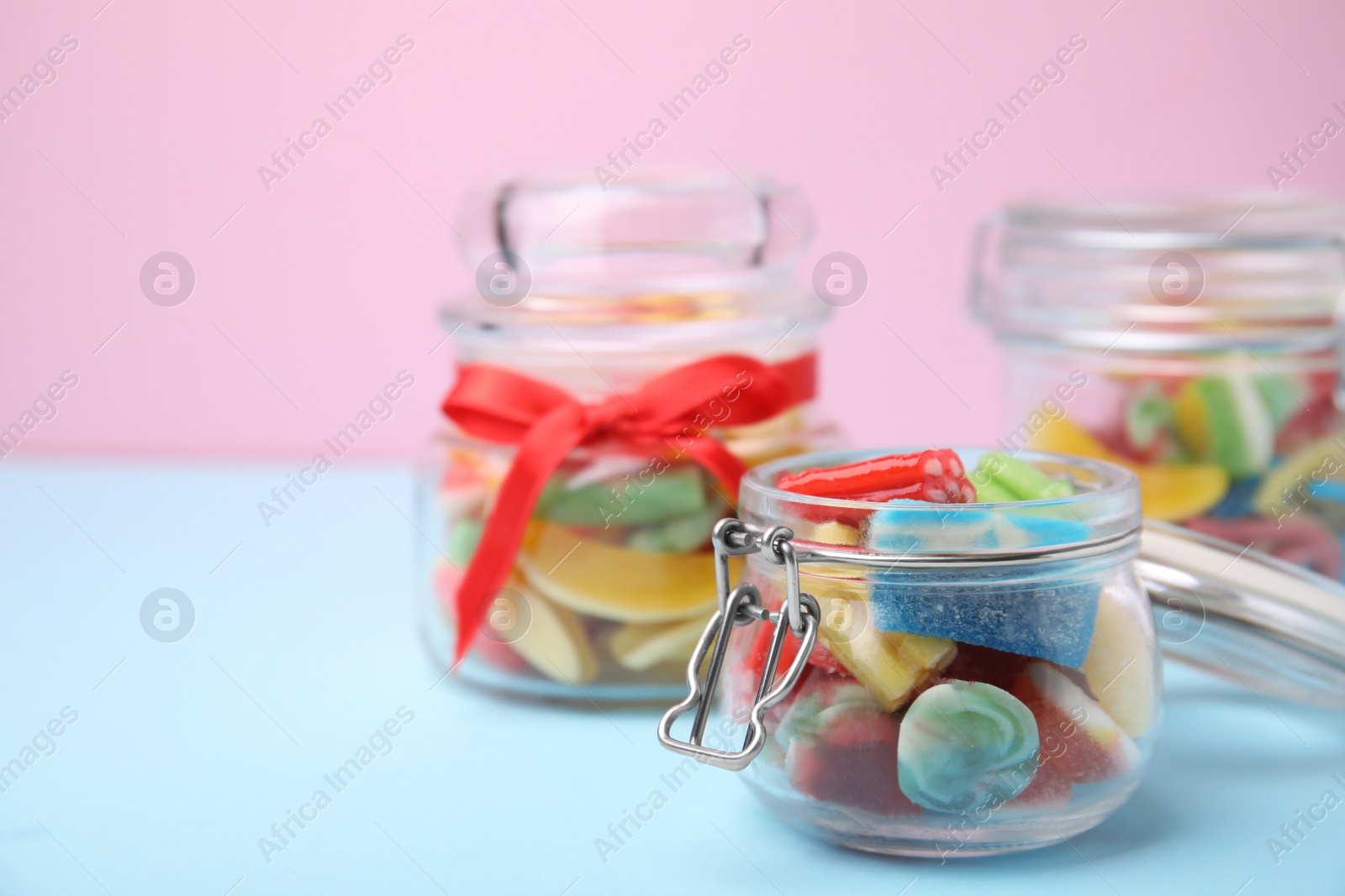 Photo of Tasty colorful jelly candies in glass jars on light blue table against pink background. Space for text