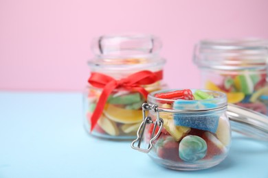 Tasty colorful jelly candies in glass jars on light blue table against pink background. Space for text