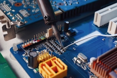 Repairing electronic circuit board with soldering iron on table, closeup