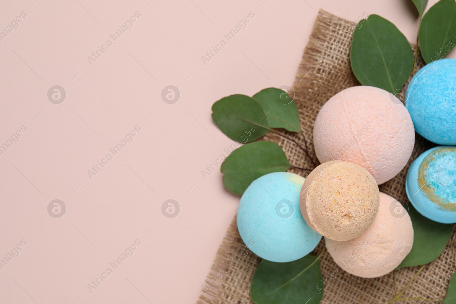 Photo of Bath bombs, eucalyptus leaves and burlap fabric on beige background, flat lay. Space for text