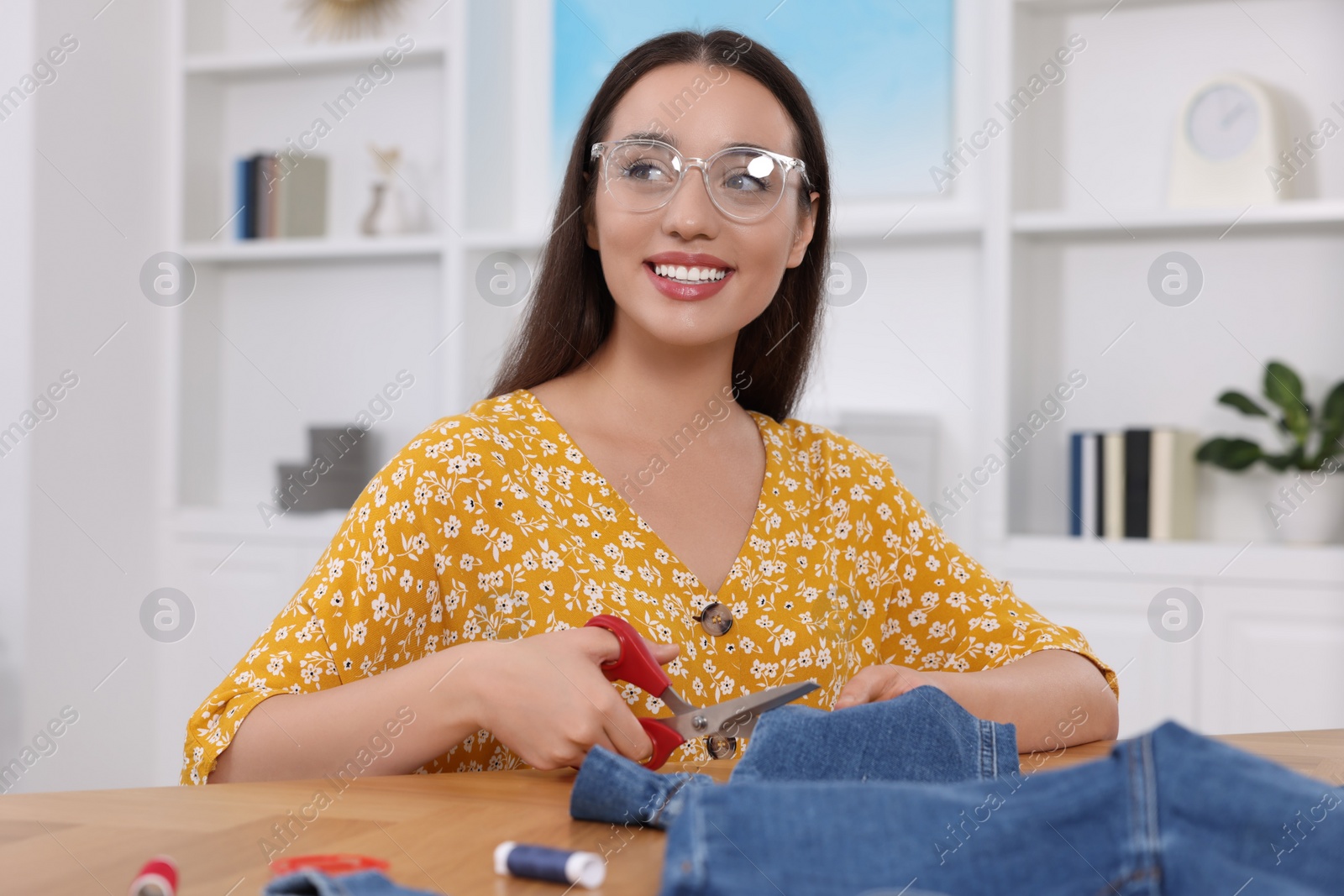 Photo of Happy woman cutting hem of jeans at table indoors