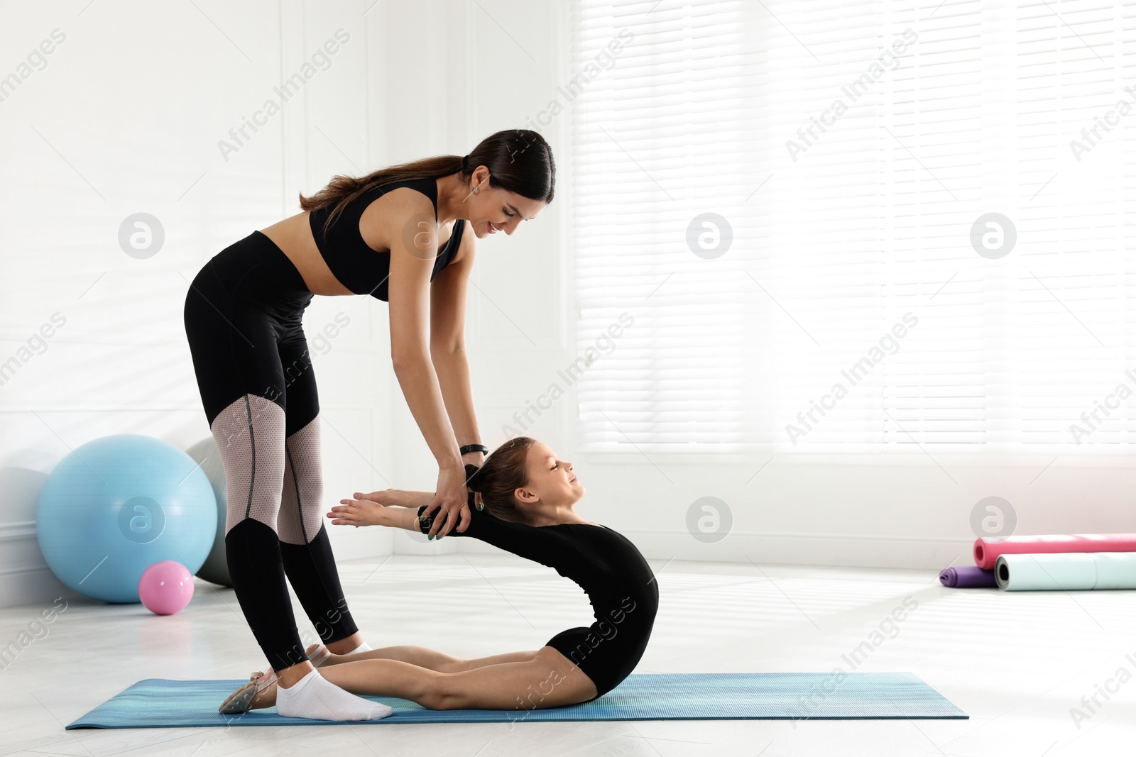 Photo of Gymnastic coach helping little girl to stretch indoors