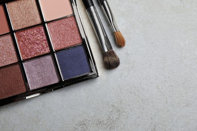 Beautiful eye shadow palette and brushes on grey table, flat lay. Space for text