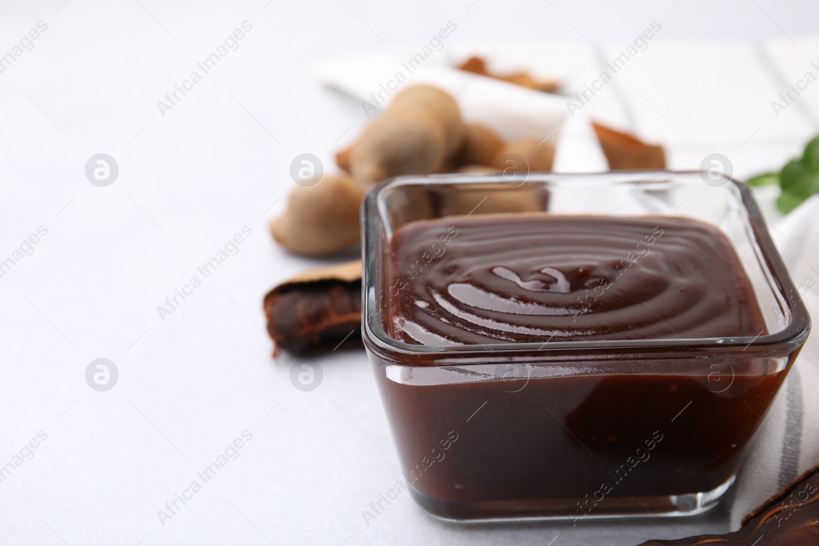 Bowl of tasty tamarind sauce and fresh pods on light table. Space for text Photo of Bowl of tasty tamarind sauce and fresh pods on light table. Space for text