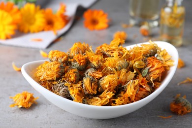 Photo of Plate of dry calendula flowers on grey table, closeup