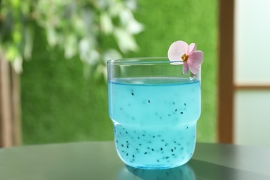 Tasty light blue drink with basil seeds on table