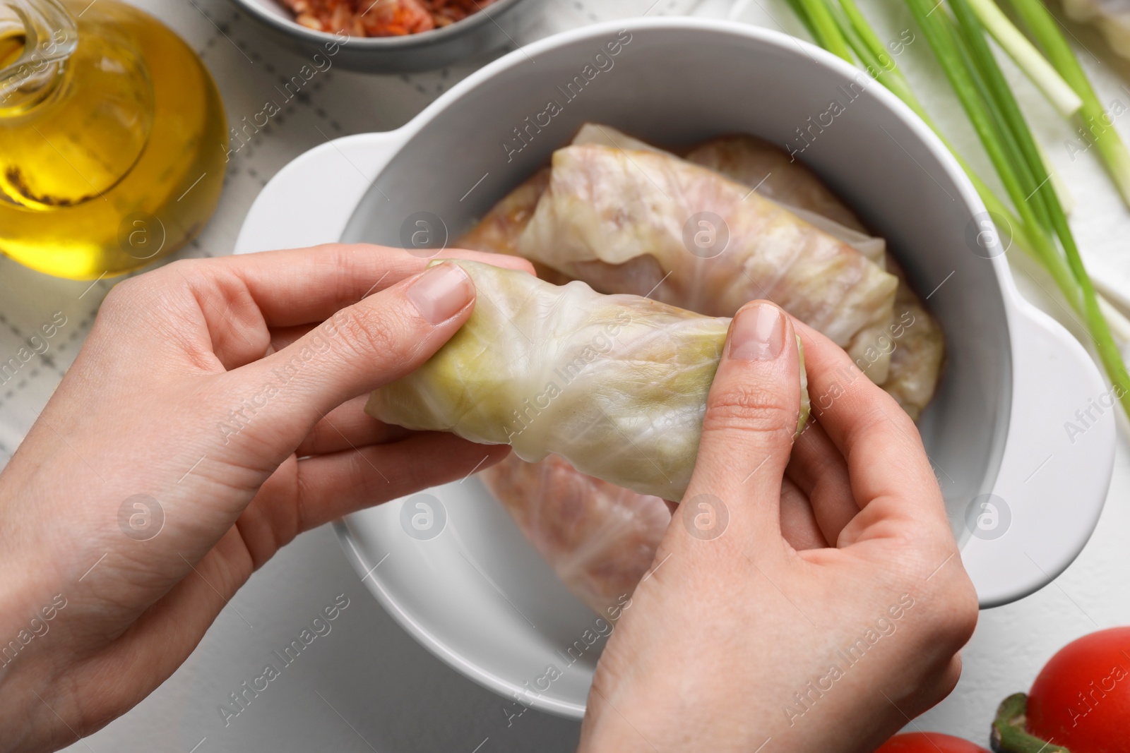 Photo of Woman putting uncooked stuffed cabbage roll into ceramic pot at table, top view