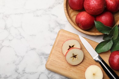 Photo of Ripe red apples, knife and green leaves on white marble table, flat lay. Space for text