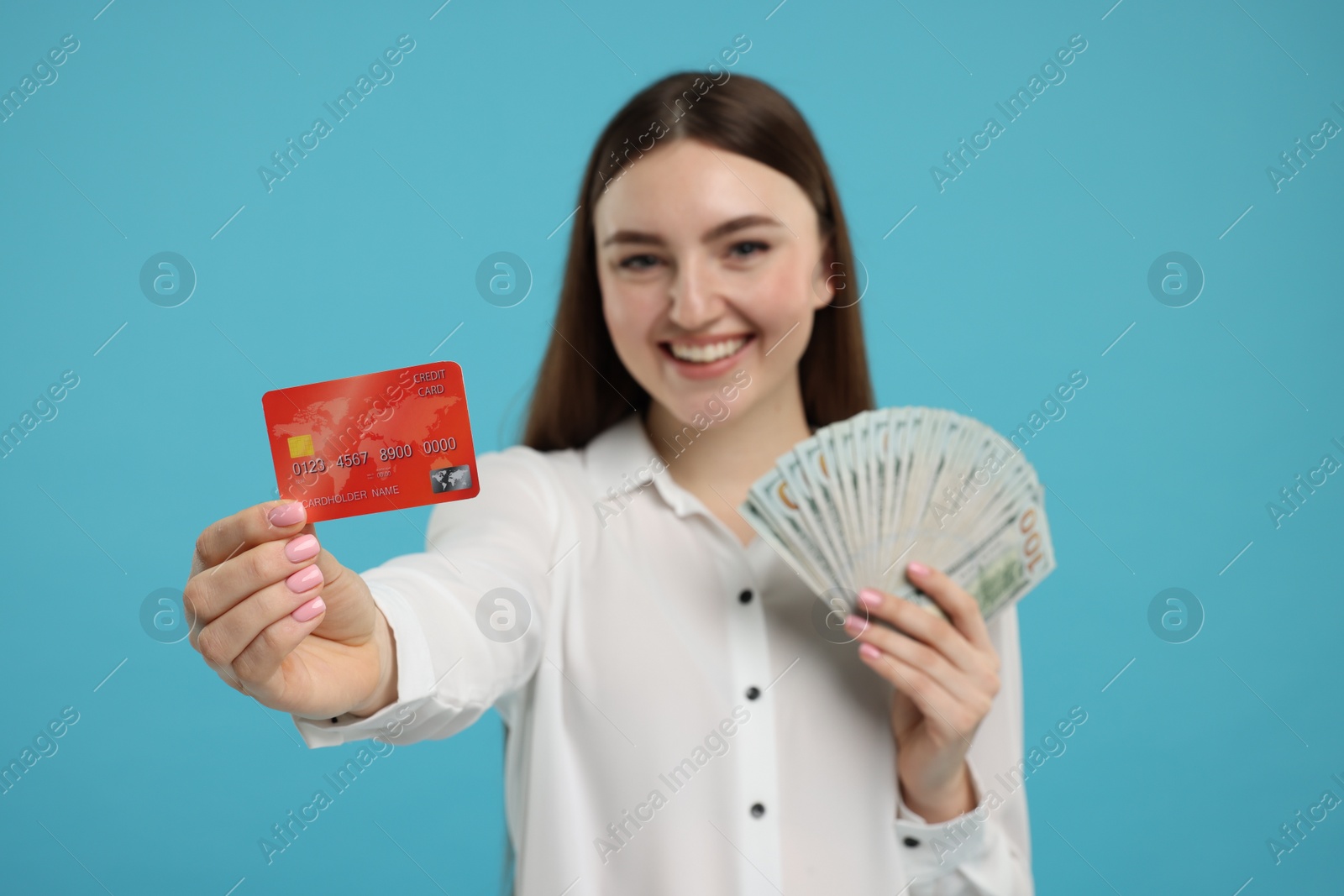 Photo of Happy woman with credit card and dollar banknotes on light blue background, selective focus