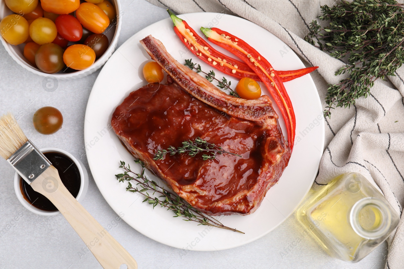 Photo of Raw marinated meat with thyme, chili pepper and basting brush on light table, flat lay