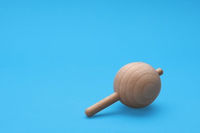 One wooden spinning top on light blue background, space for text. Toy whirligig