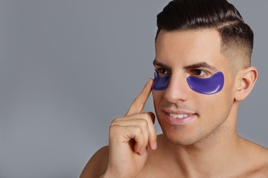 Man applying blue under eye patch on grey background. Space for text