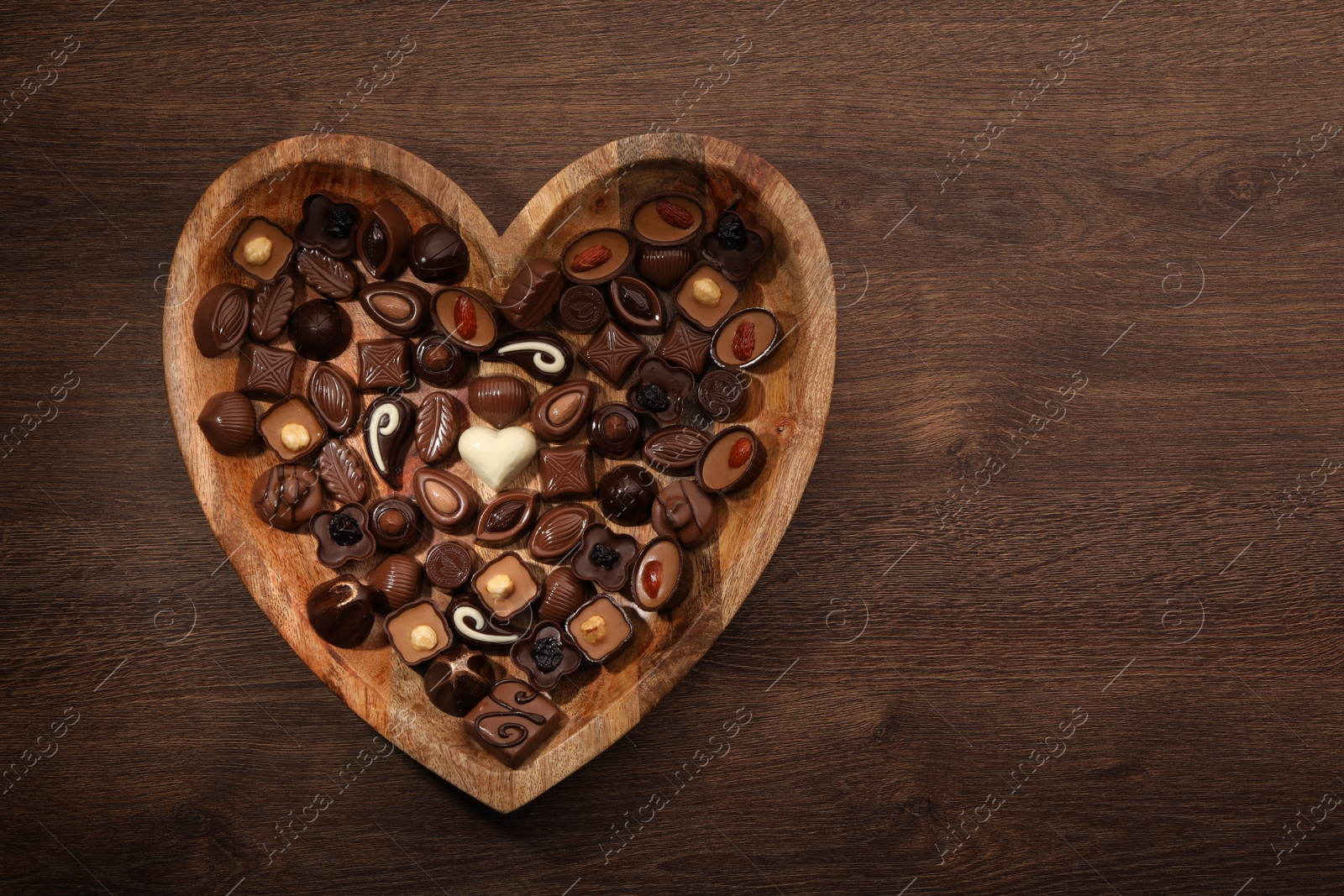 Photo of Heart shaped plate with delicious chocolate candies on wooden table, top view. Space for text