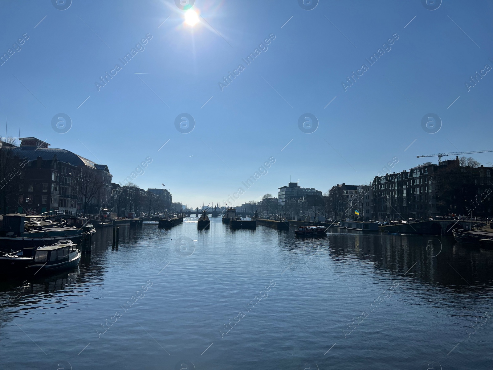 Photo of Amsterdam, Netherlands - March 01, 2023: Picturesque view of river embankment with moored boats in city under blue sky