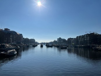 Photo of Amsterdam, Netherlands - March 01, 2023: Picturesque view of river embankment with moored boats in city under blue sky