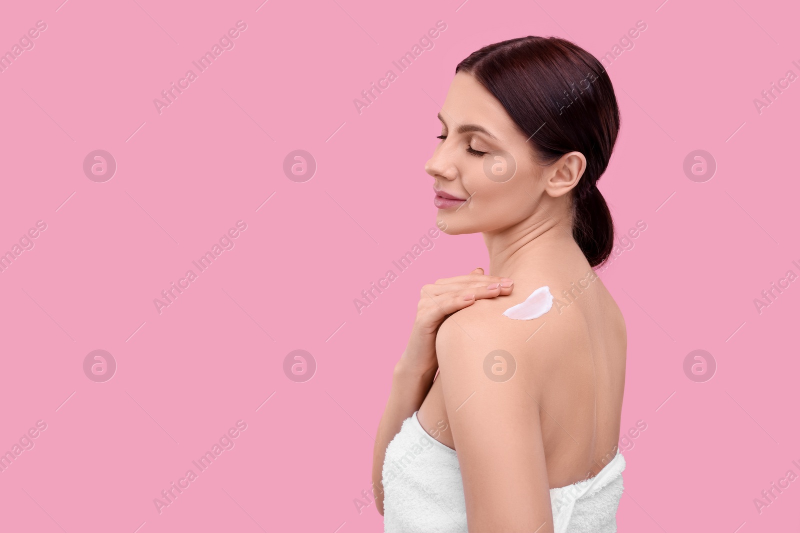 Photo of Beautiful woman with smear of body cream on her shoulder against pink background, space for text