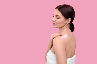 Beautiful woman with smear of body cream on her shoulder against pink background, space for text