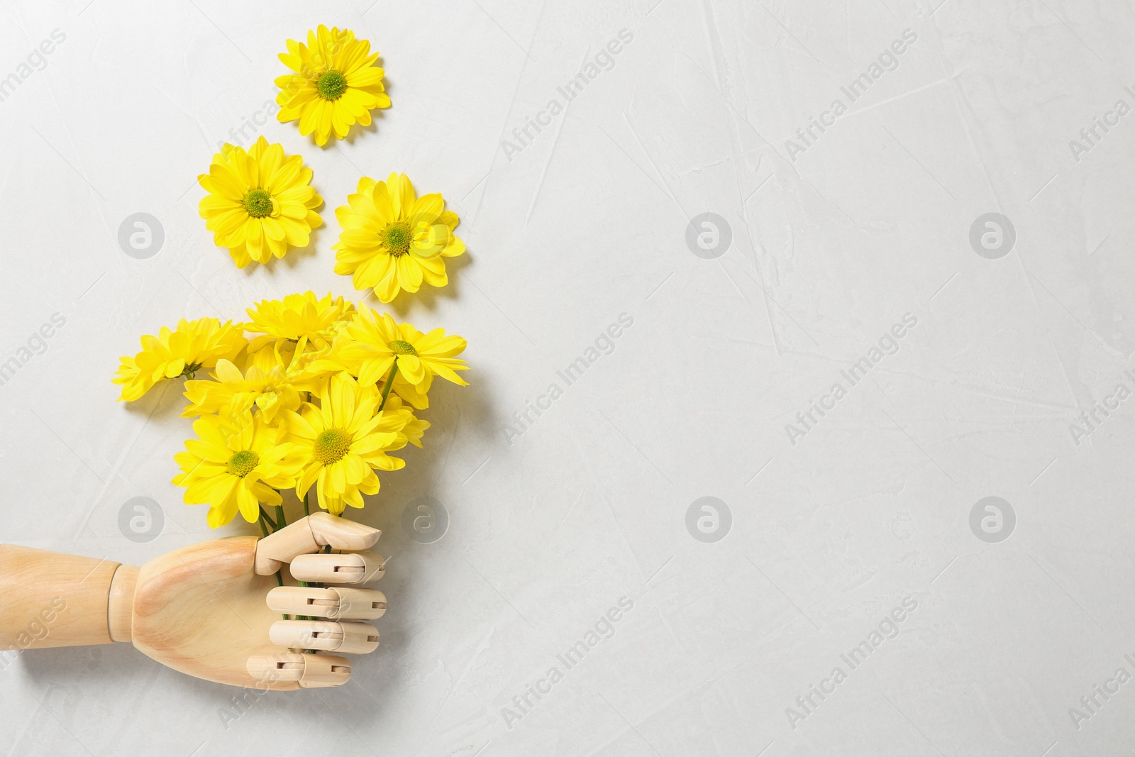 Photo of Wooden mannequin hand and yellow flowers on white background, flat lay. Space for text