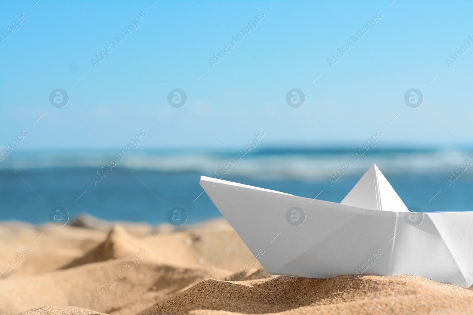 Photo of White paper boat near sea on sunny day, closeup. Space for text