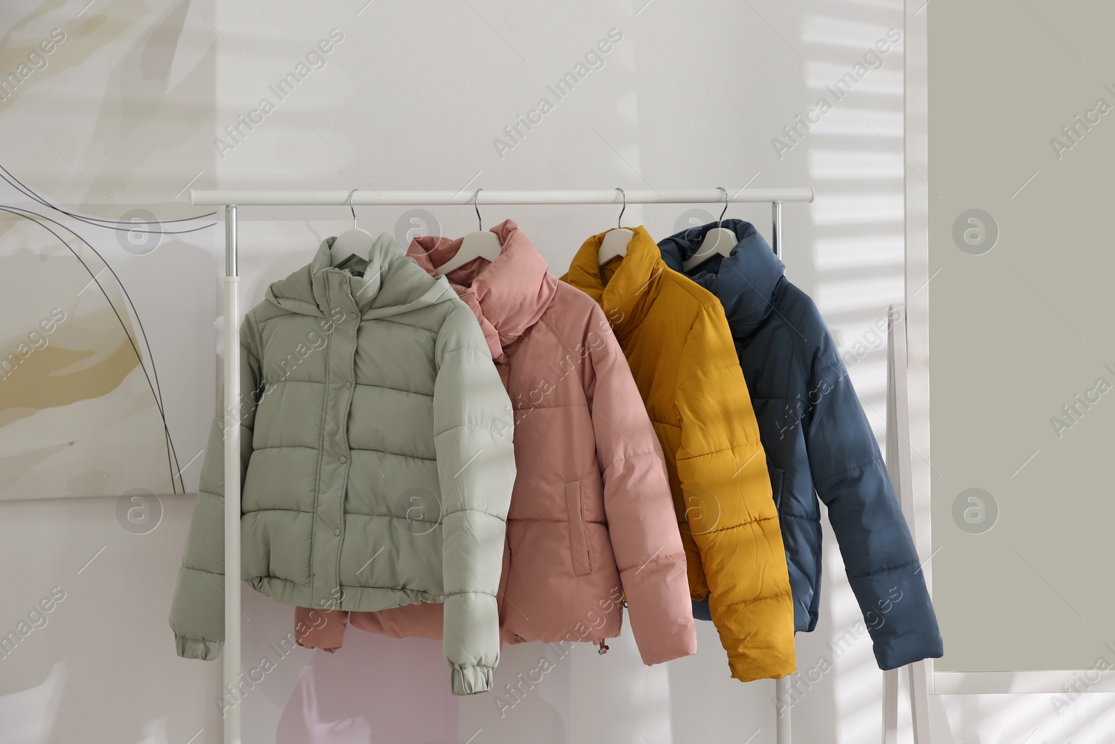 Photo of Different warm jackets hanging on rack indoors