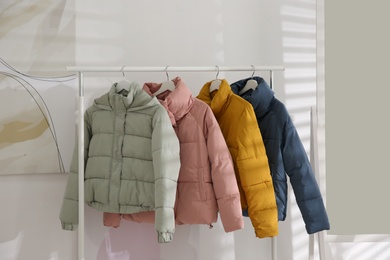 Different warm jackets hanging on rack indoors