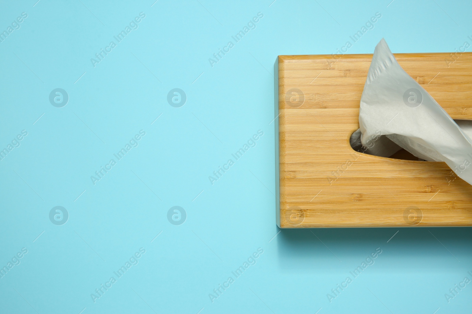 Photo of Wooden holder with paper tissues on light blue background, top view. Space for text