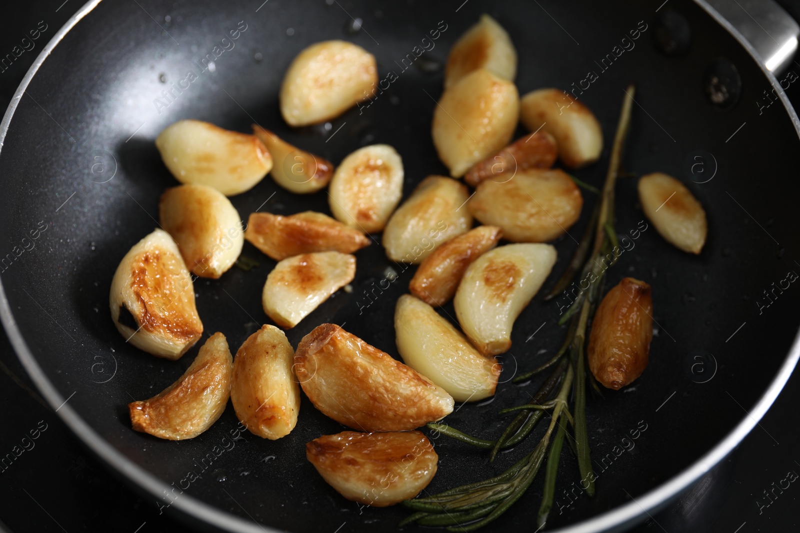 Photo of Frying pan with fried garlic cloves and rosemary, closeup