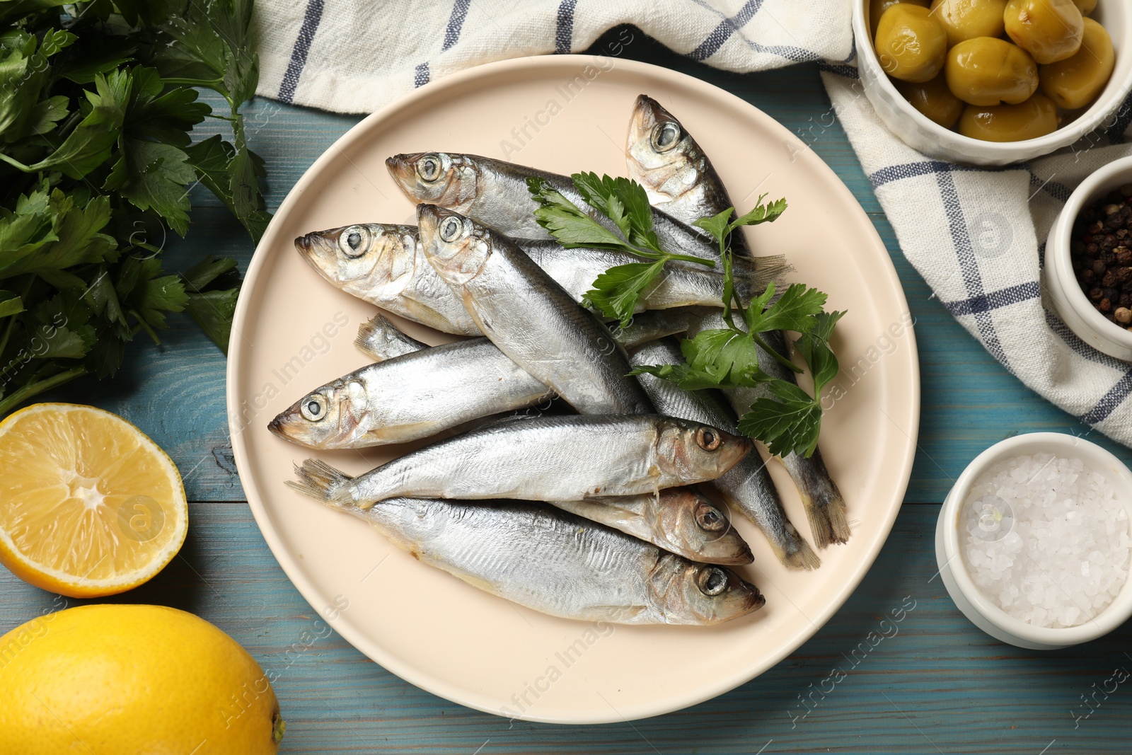 Photo of Fresh raw sprats, parsley and other products on light blue wooden table, flat lay