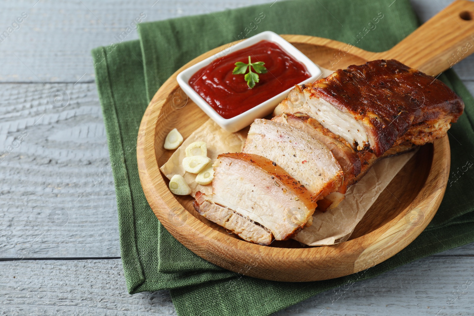 Photo of Pieces of baked pork belly served with sauce on grey wooden table