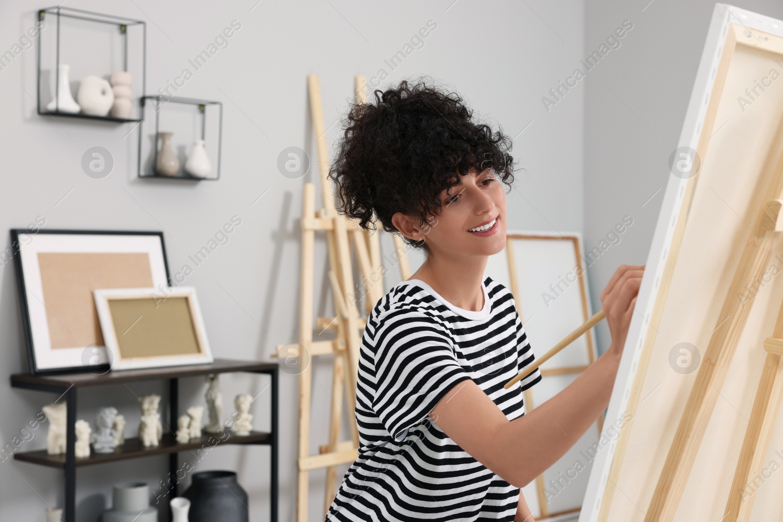 Photo of Young woman painting on easel with canvas in studio