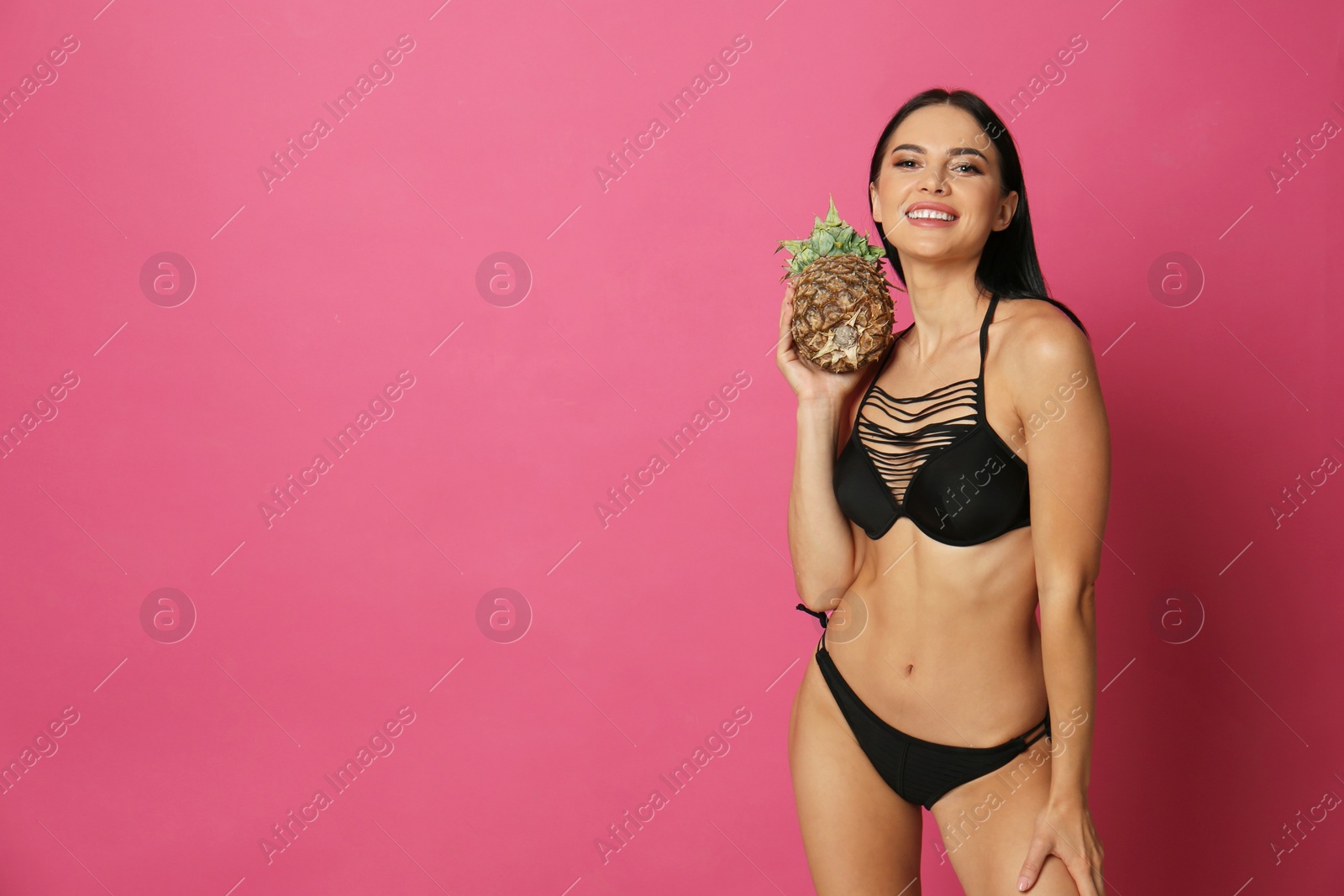 Photo of Beautiful young woman in black bikini with pineapple on pink background. Space for text