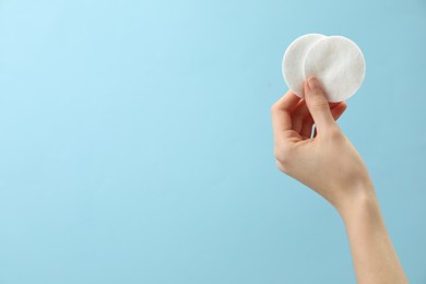 Woman holding cotton pads on light blue background, closeup. Space for text