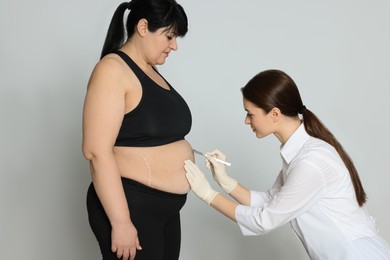 Photo of Doctor with scalpel near obese woman on light background. Weight loss surgery
