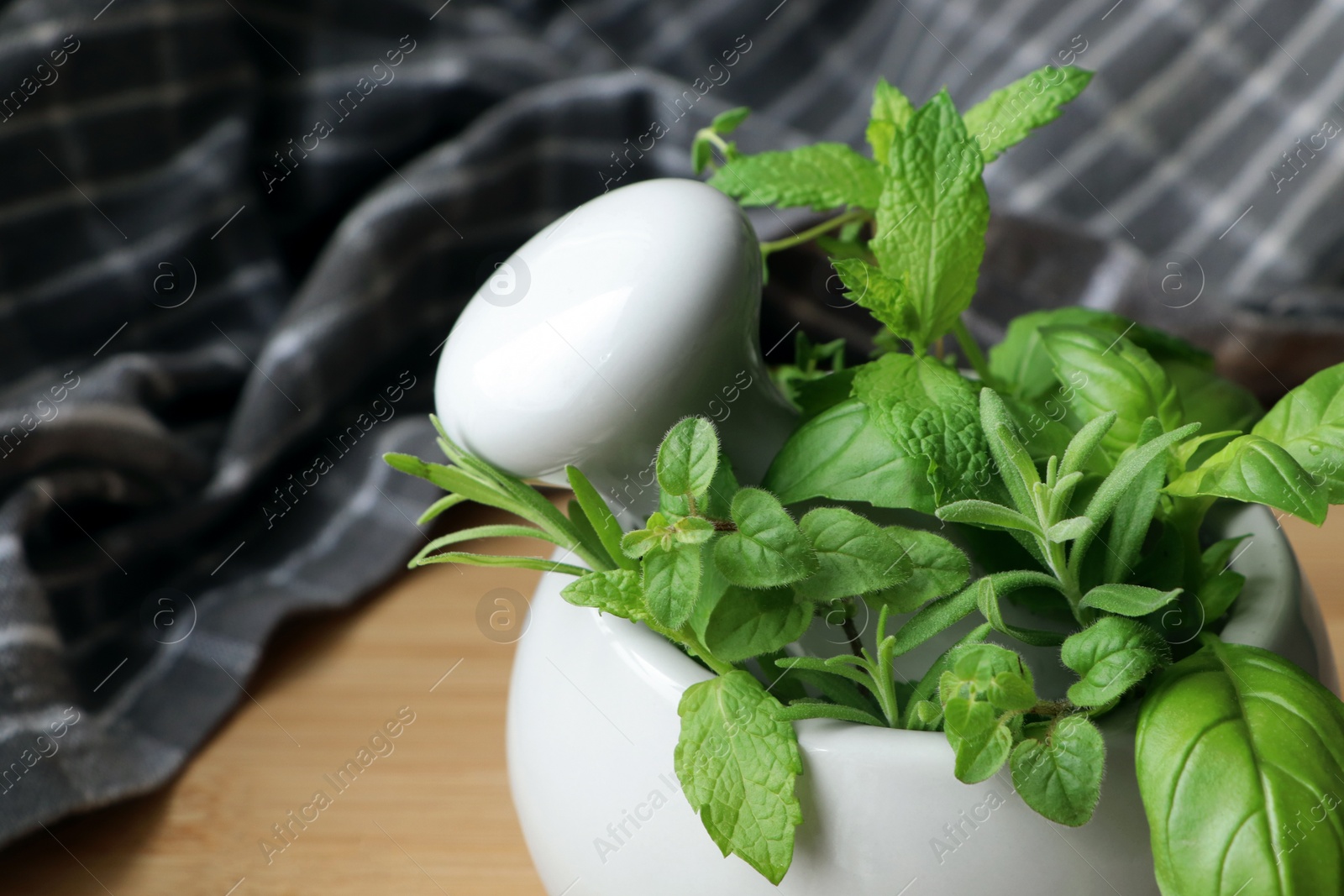 Photo of Mortar with different fresh herbs on wooden table, closeup