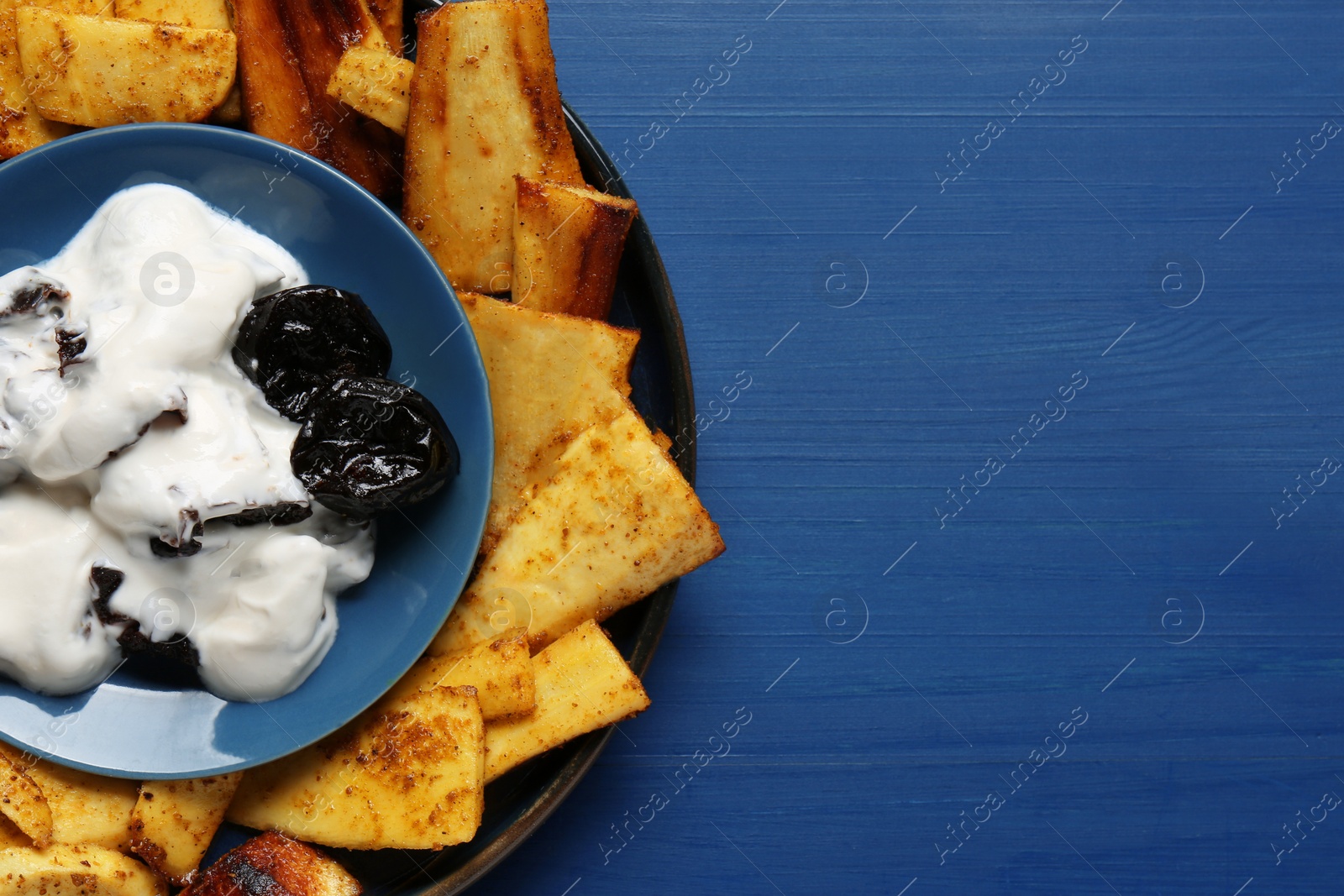 Photo of Delicious parsnips and prunes in cream sauce on blue wooden table, top view. Space for text