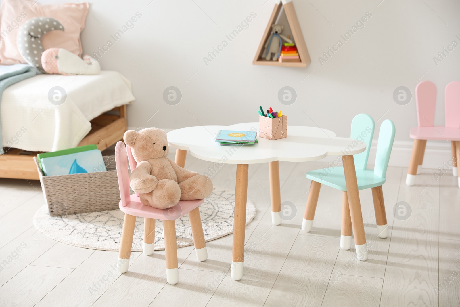 Photo of Small table and chairs with bunny ears in children's room interior