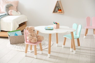 Photo of Small table and chairs with bunny ears in children's room interior