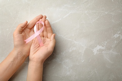 Photo of Woman holding pink ribbon on grey background, top view with space for text. Breast cancer awareness concept