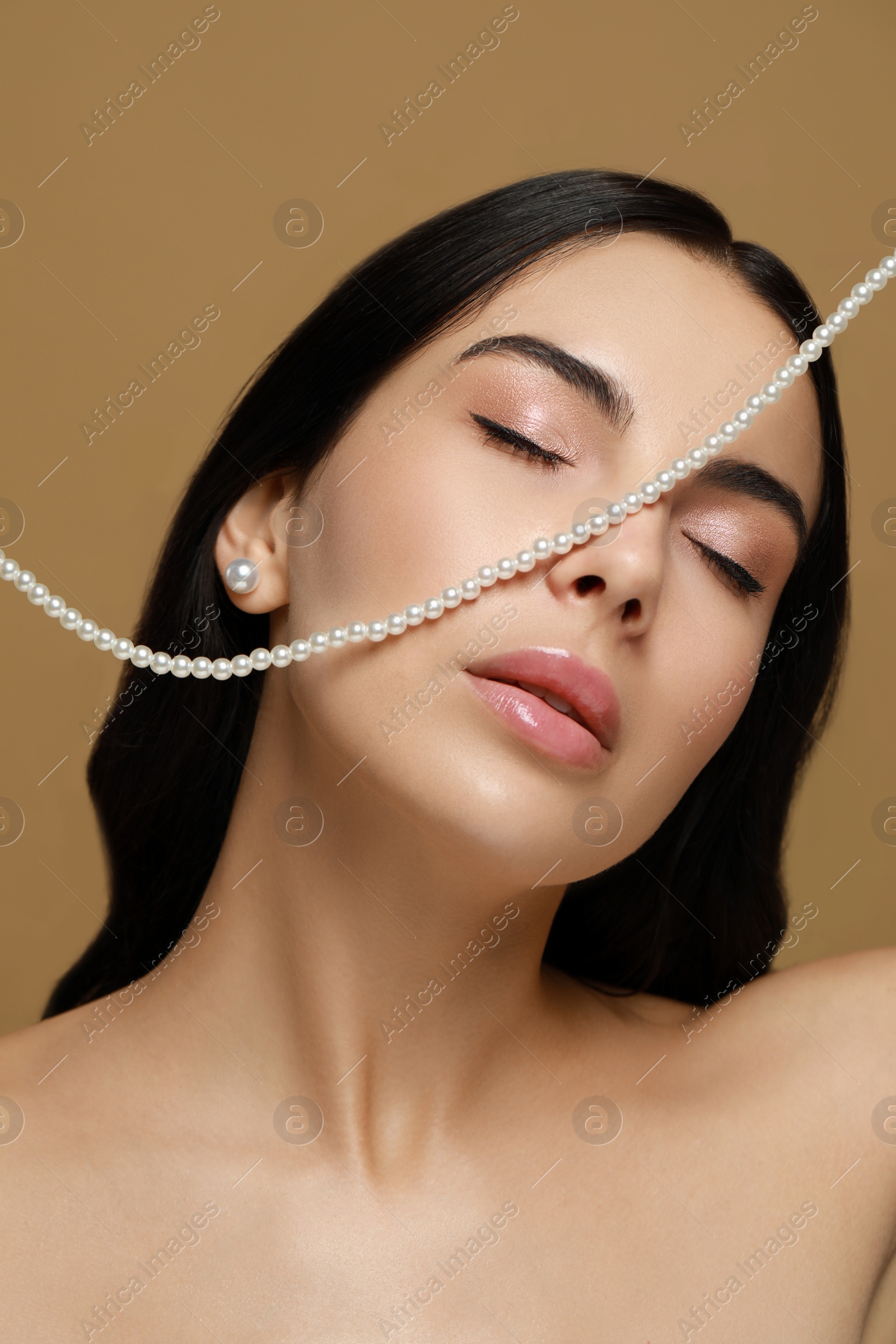 Photo of Young woman with elegant pearl jewelry on brown background, closeup