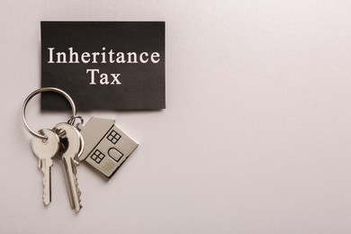 Photo of Card with phrase Inheritance Tax and keys with house shaped key chain on grey background, top view. Space for text