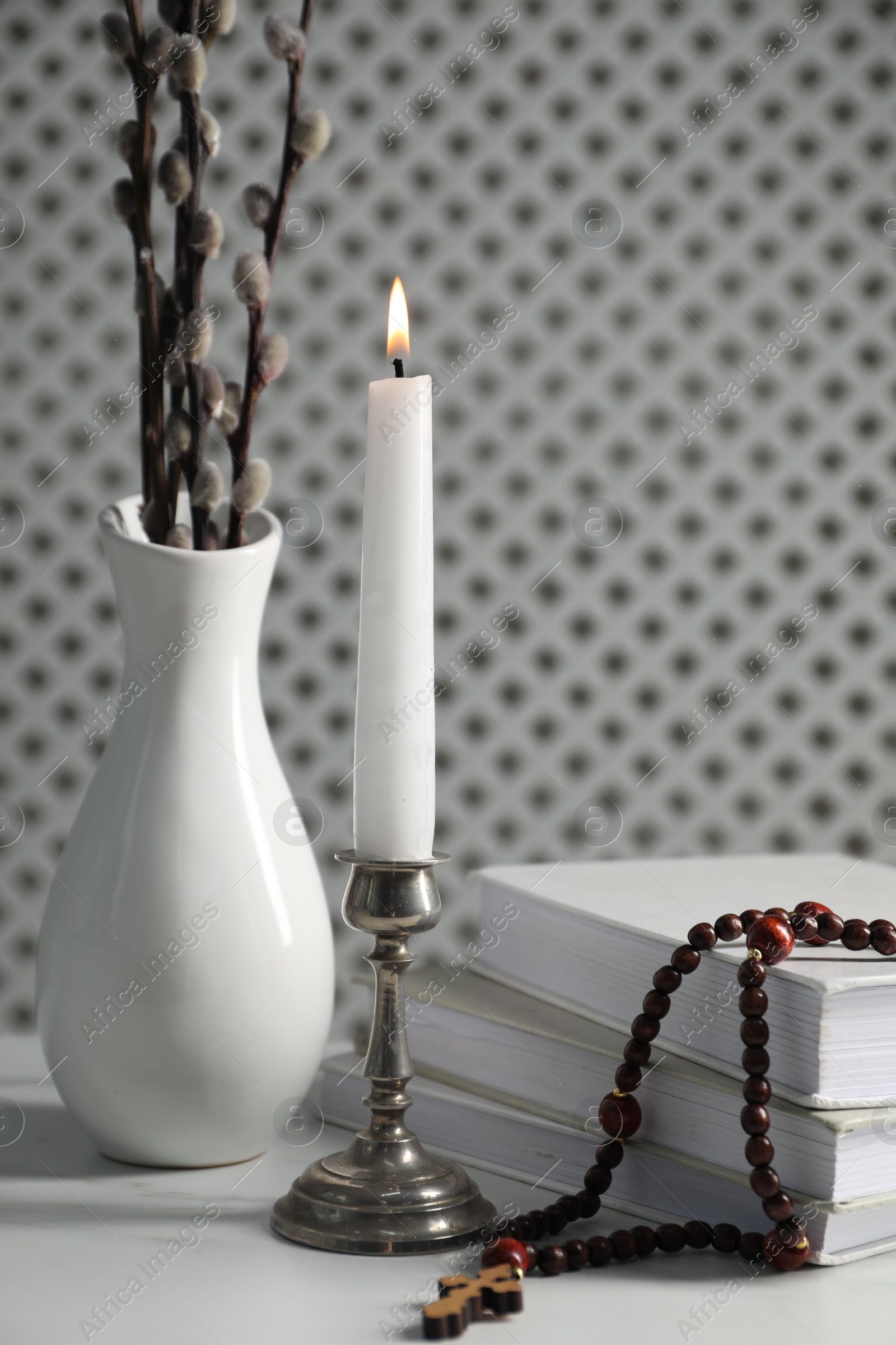 Photo of Books, burning candle, rosary beads and vase of willow branches on white table, closeup